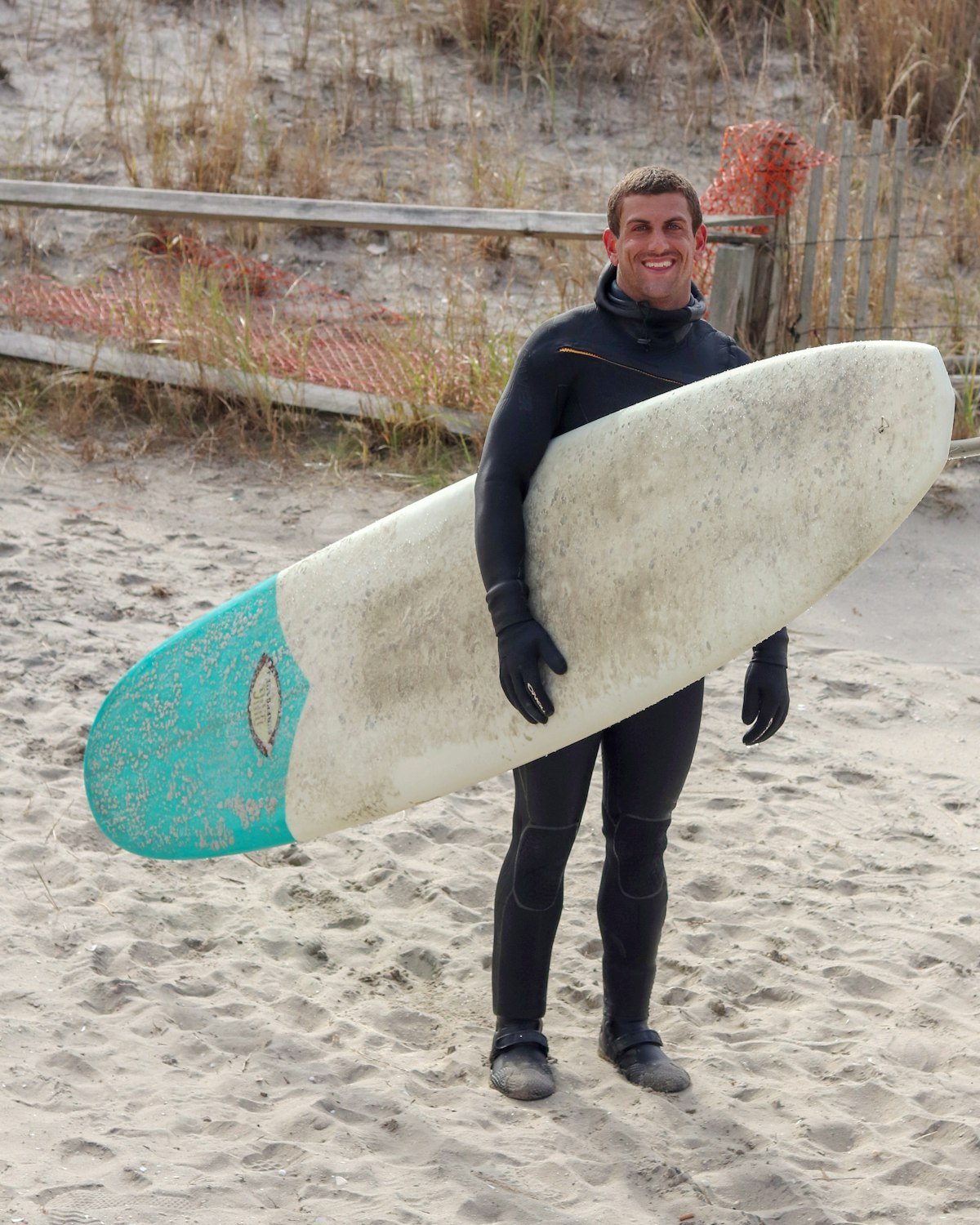 Surfer in a black wetsuit holding his board on the beach