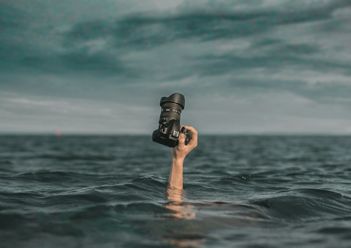 Photographer floating in the ocean, holding his camera above the water