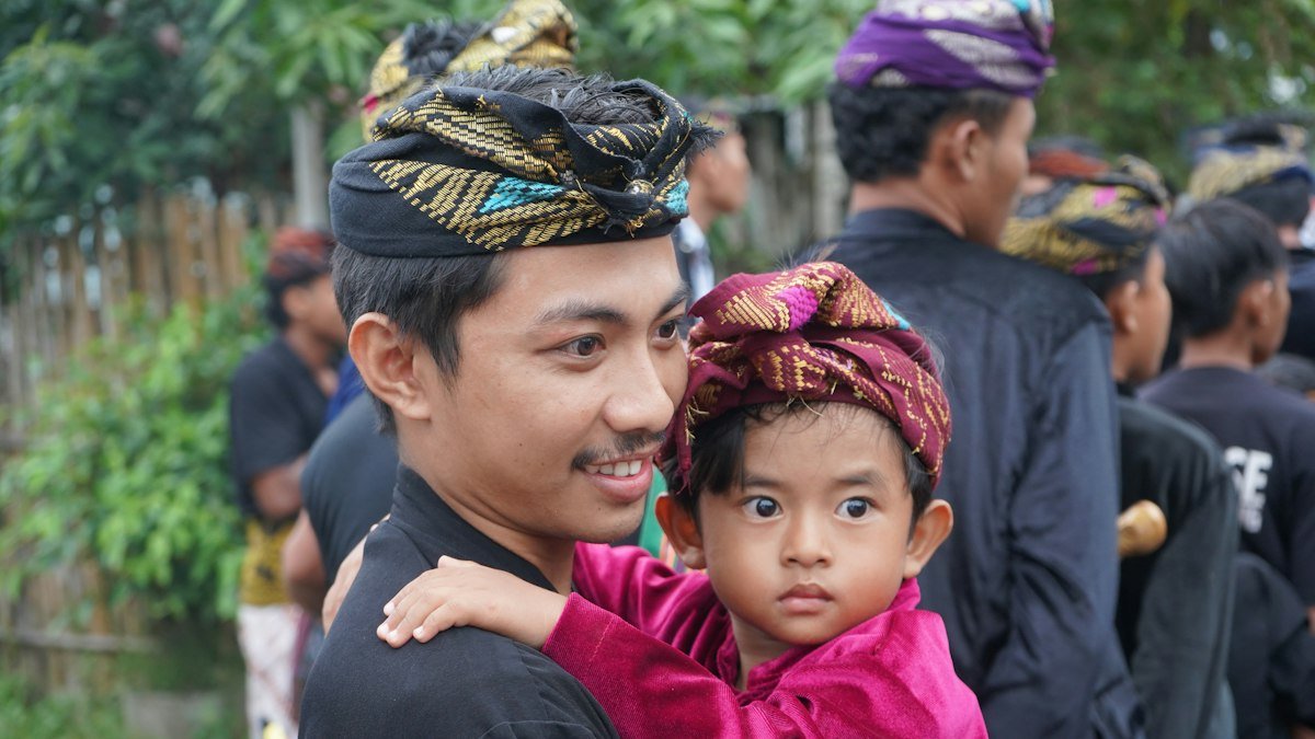 A man carrying a child wearing a traditional headdress